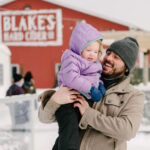 Man holding a smiling toddler in winter outside the Blake's Hard Cider barn